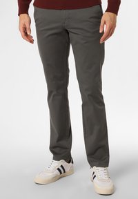 Dunkelgraue Chinos mit einer glatten Textur, schlanker Passform und seitlichen Taschen. Getragen mit weißen Sneakers mit schwarzen Streifen.
