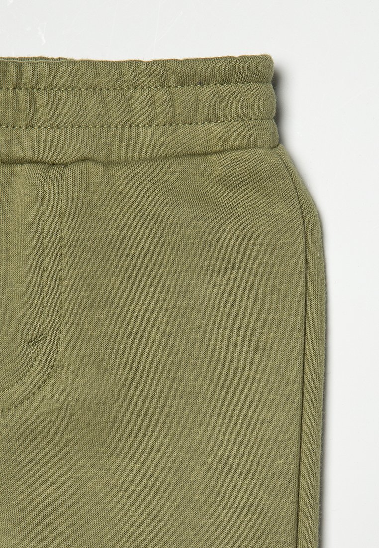 Primo piano di un tessuto verde oliva che mostra l'elastico in vita e la cucitura della tasca laterale su pantaloni casual o pantaloni della tuta.