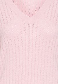 Pull en maille rose clair avec un décolleté en V, texture à côtes verticales et petits détails en mailles ouvertes sur toute la surface.