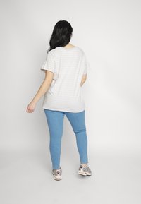 Stripet kortærmet t-shirt i lyse farver, parret med tætsiddende blå jeans og sneakers, fanget fra ryggen mod en lys baggrund.