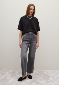Zwarte oversized t-shirt, hooggetailleerde grijze wijde jeans en zwarte instapschoenen. Glad materiaal en losse pasvorm met eenvoudige ontwerpdetails.