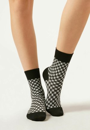 Schwarz-weiße karierten Knöchelsocken mit einem gerippten Bündchen und einer glatten Textur. Das Muster besteht aus kleinen Quadraten.
