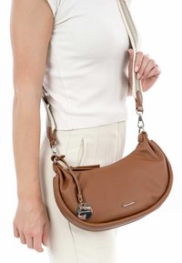 Brown leather handbag with a semi-circular shape, textured surface, and a braided strap. Features a branded metal tag and side detail.
