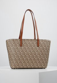 Sac fourre-tout beige avec un motif répétitif, anses en cuir marron clair, forme structurée et texture lisse. Convient pour une utilisation quotidienne.