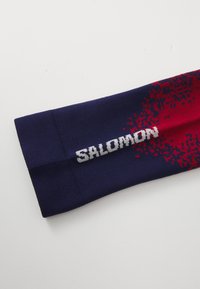 Salomon athletic arm sleeve in navy blue with red pixelated pattern, featuring a white logo. Made of textured, flexible material.