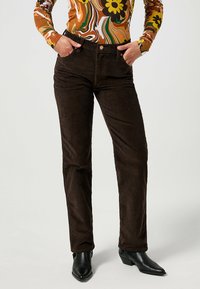 Bruna kordbyxor med figursydd midja och rak bendesign, med subtil ribbad textur och klassisk fickdetaljering.