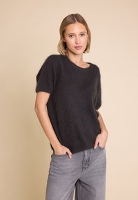 Kortermet, mørkegrå strikkegenser laget av mykt materiale, med løs passform og rund hals, kombinert med lysegrå jeans.