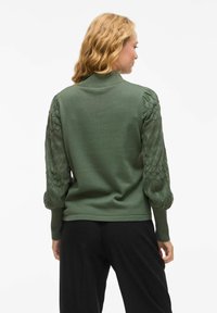 Groene trui met een slim-fit lichaam en geplooide, getextureerde mouwen met een geometrisch patroon. Ribgebreide kraag en manchetten; zachte breimateriaal.