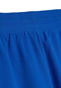 Niebieski strój z zebranym wzorem i elastycznym paskiem w talii. Posiada wytłoczony logo "DIVERSE" na pasku. Miękka, gładka tekstura.