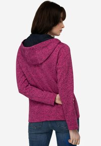 Rosa huva jacka med ett strukturerat mönster, med ett mörkt vadderat foder, långa ärmar och en avslappnad passform, kombinerad med blå jeans.