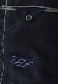 Marineblauer Stoff mit einem dezenten Muster, versehen mit einem Knopf und einem Etikett mit der Aufschrift "Calvino Vitale, hergestellt in Europa." Abgesetzt mit hellgrauen Akzenten.