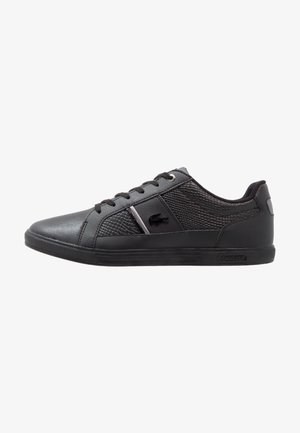 Sneaker nere con una finitura opaca liscia, dettagli testurizzati, punta rotonda, design con lacci e un dettaglio in metallo con il logo sul lato.