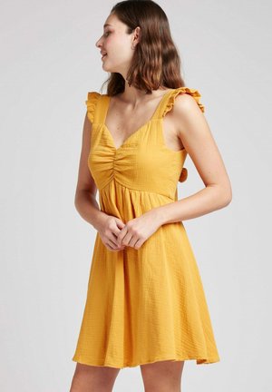 Robe d'été jaune en tissu texturé, avec des bretelles froncées, un corsage froncé et une jupe évasée.