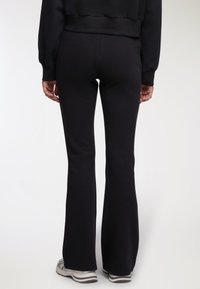 Czarne szerokie dresy wykonane z miękkiego materiału, z wysokim stanem i gładką fakturą, połączone z szarymi trampkami.