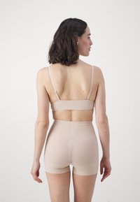 Nude, seamless bralette with adjustable straps paired with high-waisted, sheer boyshorts. Smooth texture, minimalist design, and no visible seams.