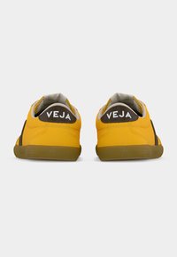 Κίτρινα αθλητικά παπούτσια με λεία υφή, καφετί λεπτομέρειες και λογότυπο "VEJA" στη φτέρνα. Στρογγυλεμένο σχήμα και καουτσουκερές σόλες για καλύτερη πρόσφυση.
