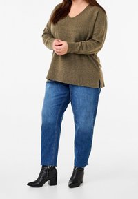 Olivgrüner Strickpullover mit V-Ausschnitt und gerippetem Saum, kombiniert mit hellblauen, geraden Jeans und schwarzen Stiefeletten.