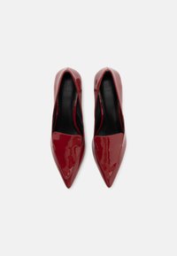 Red patent leather high heels with a pointed toe, flat vamp, and smooth texture. The interior features a black lining.