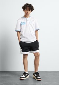 White mesh short-sleeve shirt with blue accents, number 23, black shorts with white hem and side detail, and black sneakers with white and red accents.
