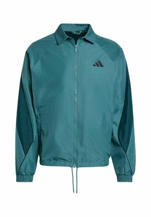 Veste légère turquoise avec fermeture éclair à l'avant, col montant, poignets élastiques et un logo noir sur la poitrine. Présente des détails de panneaux en contraste.