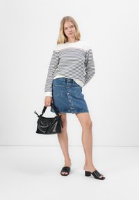 Gestreepte witte en marineblauwe trui, denim rok met knoopsluiting aan de voorkant, zwarte textuur handtas, en zwarte open teen block heel sandalen.