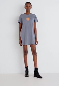Gray cotton T-shirt dress with short sleeves, featuring a centered orange sun graphic. Paired with black ankle boots, smooth texture.