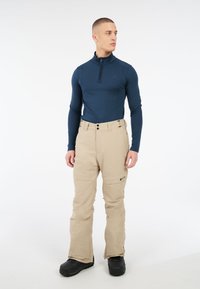 Marineblauw, lang-gevormde ritsshirt gecombineerd met beige sneeuwbroeken, voorzien van zakken en een comfortabele pasvorm, gedragen met zwarte laarzen.