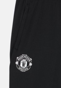 Melnas sporta šortus ar gludu tekstūru, kreisajā pusē ir balts "Manchester United" logotips. Vienkāršs dizains, bez papildus rakstiem.