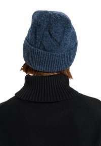 Mørkeblå strikket hue med ribbet kant og struktureret mønster på toppen. Båret med en højhalset sort sweater, der viser en blød stoffinish.