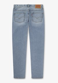 Jean en denim bleu clair avec une coupe droite, comportant deux poches arrière et une étiquette en cuir marron au niveau de la taille. Détails de couture classiques.