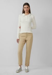 Witte geribbelde lange mouwen polo met een kraag en knoopsluiting, gecombineerd met beige tapered chino's en zilveren sportschoenen.