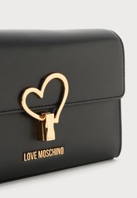 Portafoglio in pelle nera con chiusura a forma di cuore dorato e branding "LOVE MOSCHINO". Texture liscia con bordi cuciti. Design compatto e rettangolare.
