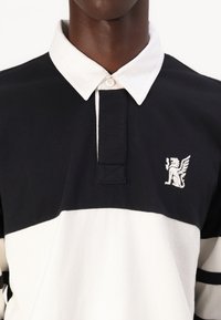 Polo shirt alb-negru cu un guler contrastant, având un mic logo brodat cu leu și un material texturat.