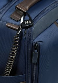 Marineblaue Reisetasche aus strukturiertem Stoff mit Lederakzenten und integriertem Zahlenschloss. Verfügt über Reißverschlüsse und ein aufgerolltes Kabel für zusätzliche Sicherheit.