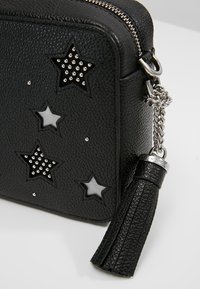 Borsa nera texturizzata con zip, caratterizzata da accenti argentati a forma di stella e strass, con dettagli a frangia e hardware argentato.