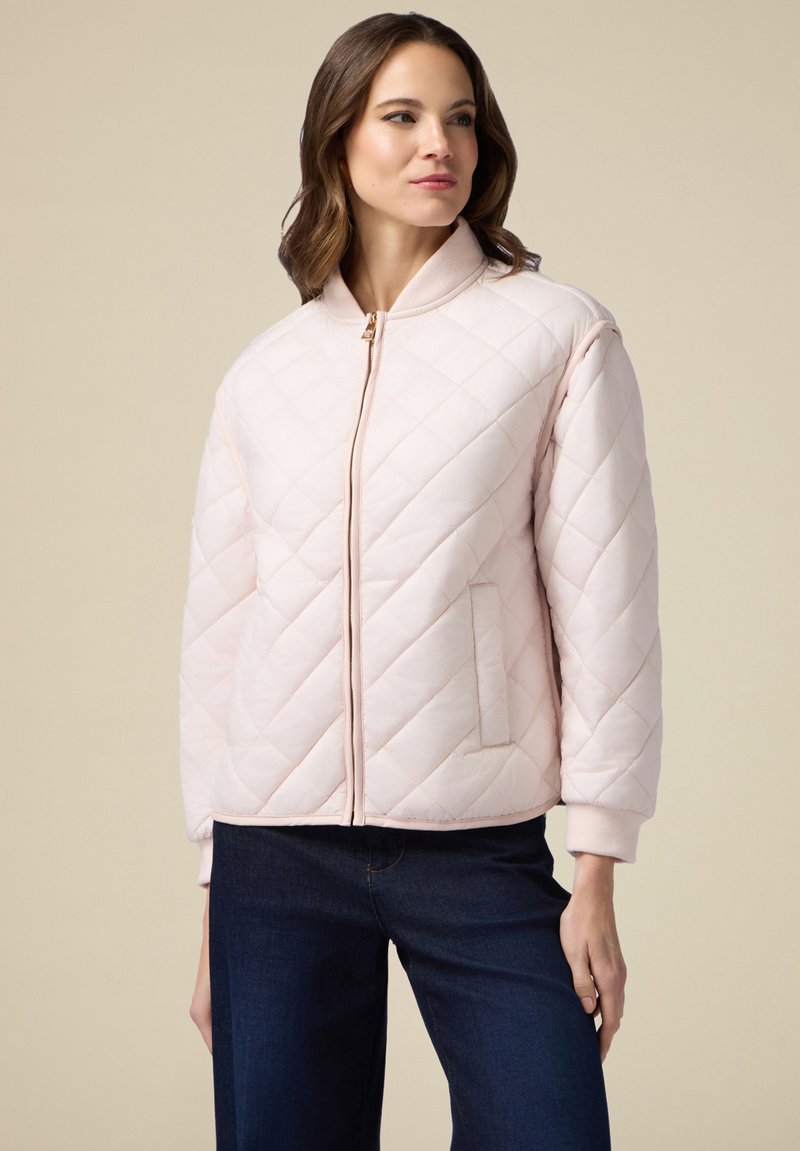 Giacca bomber trapuntata in rosa delicato. Presenta una chiusura con zip, polsini a costine e una tasca a toppa. Texture liscia con un motivo a rombi.
