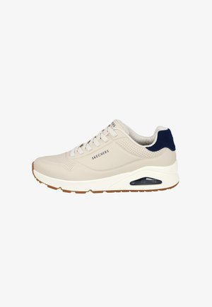 Zapatilla Skechers con parte superior de sintético beige, acento en azul marino en el talón, media suela blanca y un detalle de almohadilla de aire translúcida.