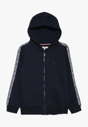 Granatowa bluza z kapturem na zamek, z białą taśmą z logo na rękawach i małym logo Tommy Hilfiger na piersi.