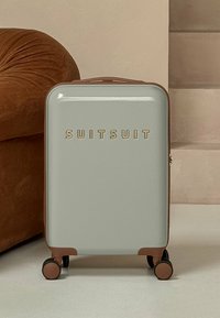 Light gray hard-shell suitcase with bronze accents, small wheels, and embossed "SUITSUIT" logo on the front. Smooth texture, compact design.
