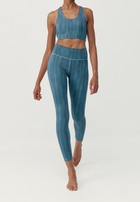 Souprava sportovního oblečení obsahující tyrkysovou sportovní podprsenku a legíny vyrobené z hladké, elastické látky s jemným barevným přechodem. Bez viditelného kování.