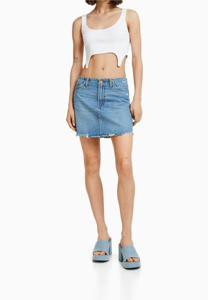 Hvid ribstrikket crop top med udskæring, kombineret med en denim mininederdel med frynset kant og lyseblå chunky sandaler med hæl.