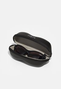 Estojo preto com zíper e interior suave, contendo óculos de sol escuros com armação preta brilhante e o logo "vogue" tanto no estojo quanto nos óculos.