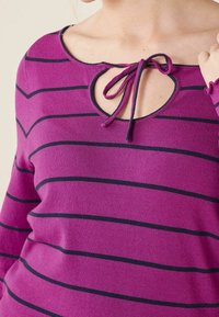 Lila gestreifter Pullover mit einem Keyhole-Ausschnitt, der mit einem Kordelzug gebunden ist. Der Stoff wirkt weich mit einer feinen Textur.