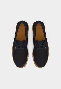 Boat παπούτσια από σκούρο μπλε δέρμα με ταμπά λαστιχένιες σόλες και μαύρα κορδόνια, απεικονιζόμενα από πάνω σε λευκό φόντο.