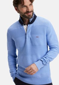 Pull en maille bleu clair avec des rayures horizontales texturées, un col marine avec un revers rayé, et un petit logo sur la poitrine.