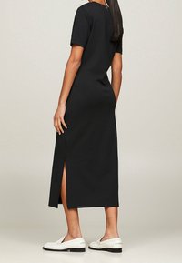 Zwart midi-jurk met korte mouwen, zachte textuur, zijslit en minimalistisch ontwerp, gecombineerd met witte loafers.