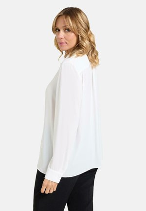 Blusa blanca de manga larga hecha de tela ligera con cuello clásico y puños con botones, presenta un corte holgado y dobladillo redondeado.