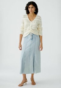 Lichtgekleurde gebreide cardigan met een V-hals en voorknoopjes, gecombineerd met een lichtblauwe denim maxi rok met zichtbare stiksels en een rafelige zoom.