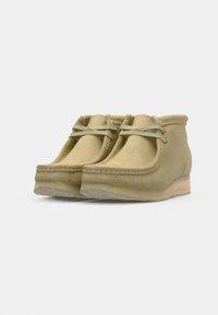 Beige suede ankle boots with a soft texture, rounded toe, and lightweight rubber sole. Features two decorative laces on the front.
