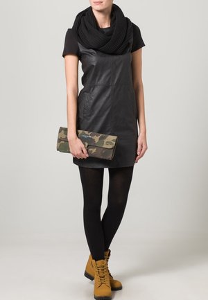 Černé kožené šaty s krátkými rukávy, žebrovaný černý šátek, černé punčocháče a hnědé boty. Drží maskáčovou kabelku s překlopným designem.